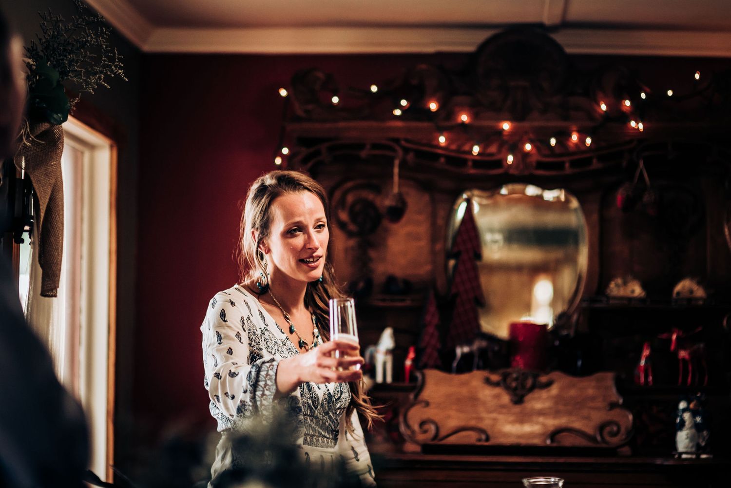Wedding guest holding champagne glass in rustic venue with string lights overhead.