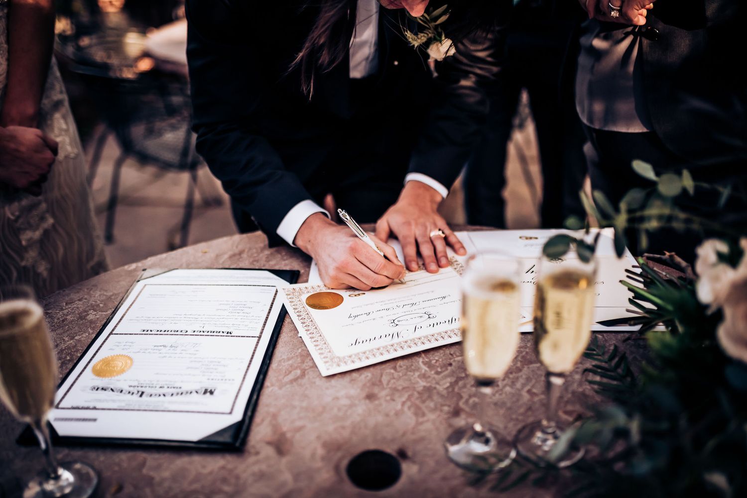 Legal documents being signed at wedding with champagne glasses on rustic table.