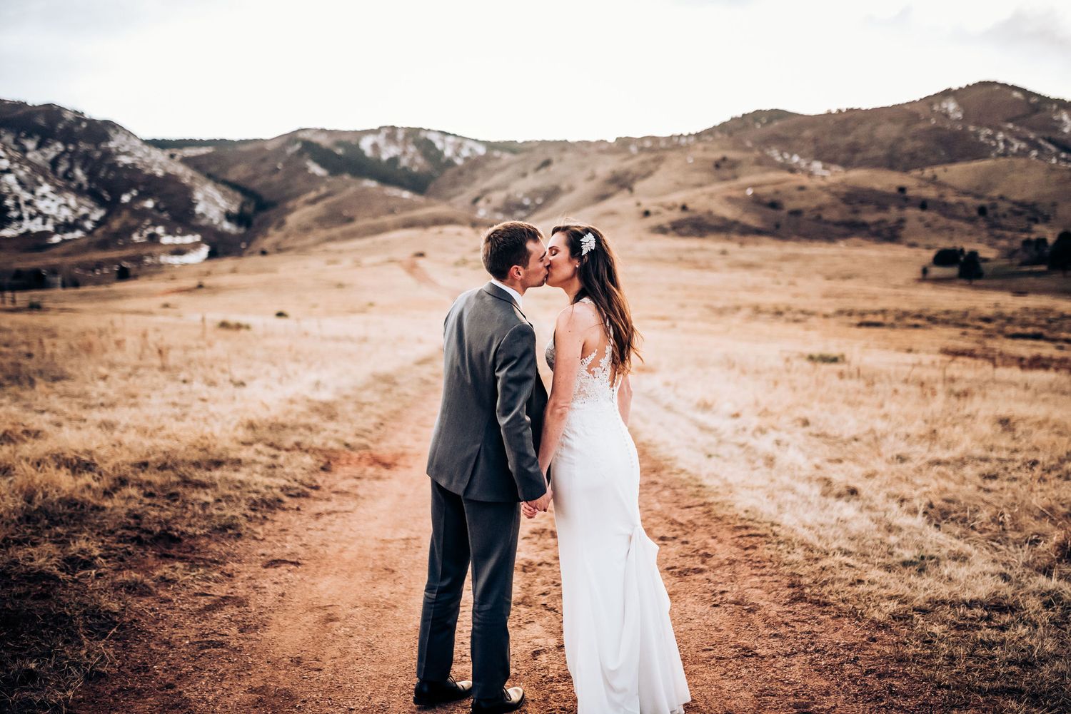 Wedding couple shares intimate moment on dirt path with rolling hills in background.