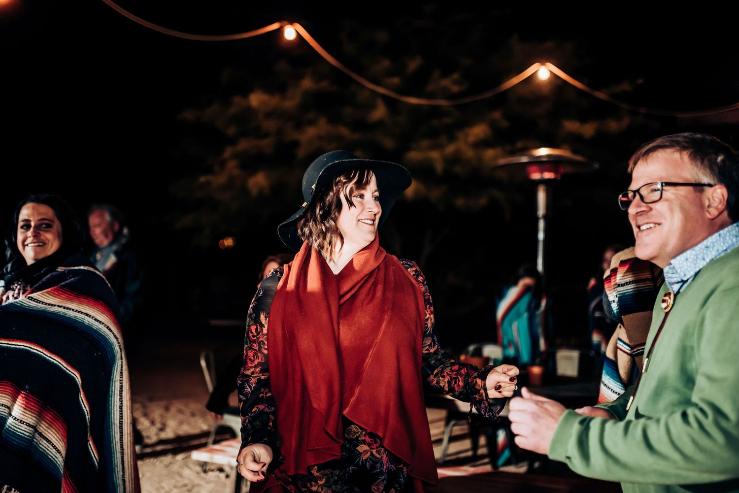 Evening outdoor gathering with string lights and patio heaters illuminating the celebration.