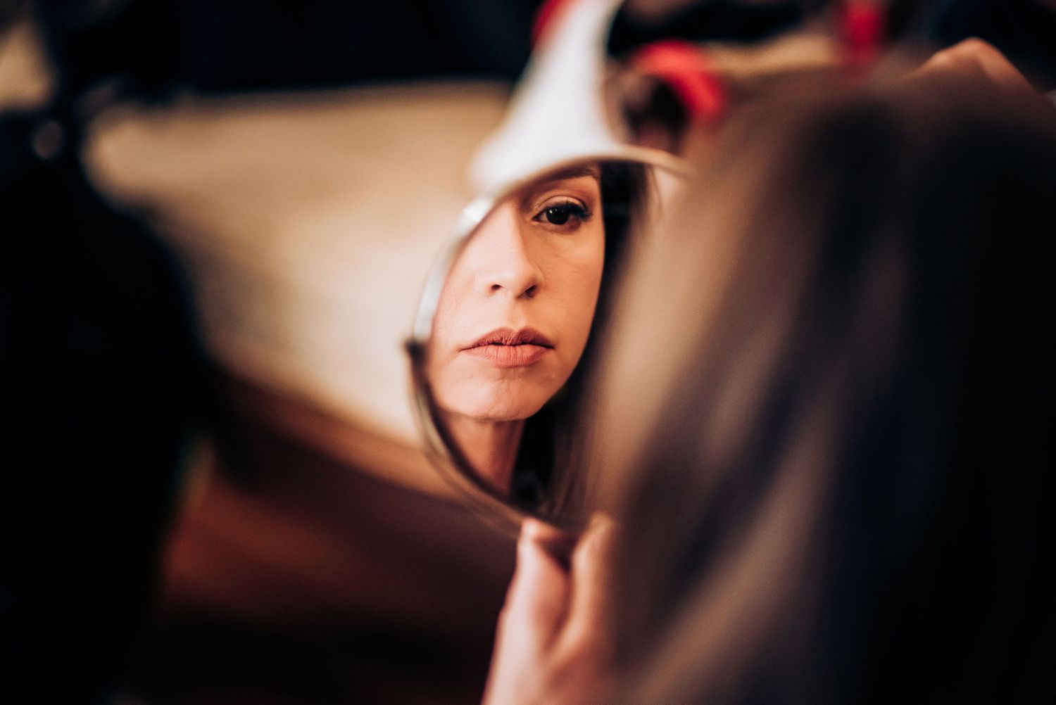 Artistic reflection of bridal makeup preparation in handheld mirror.