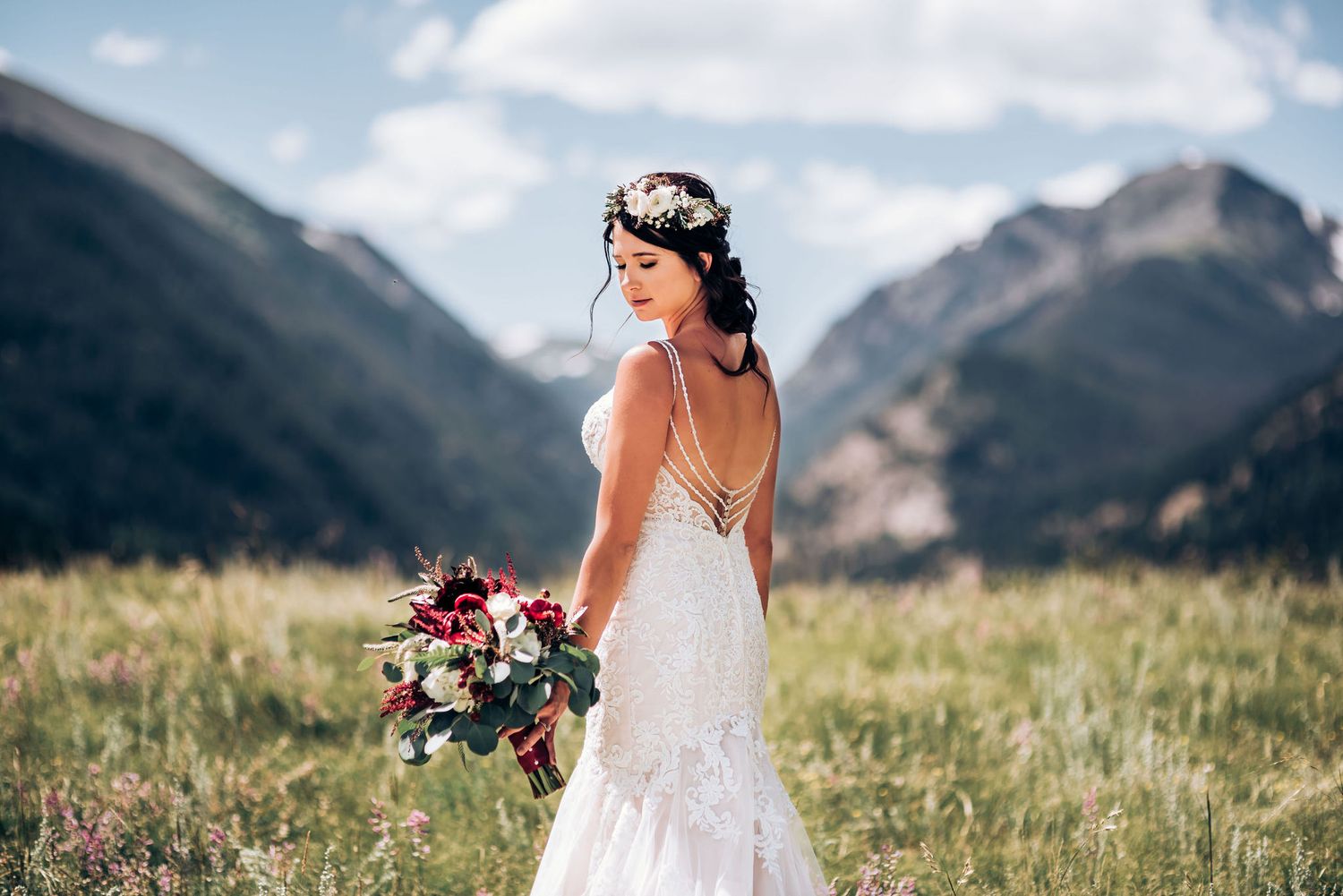 An elegant bridal portrait showcasing the low-back detail of a lace wedding gown in mountain scenery.