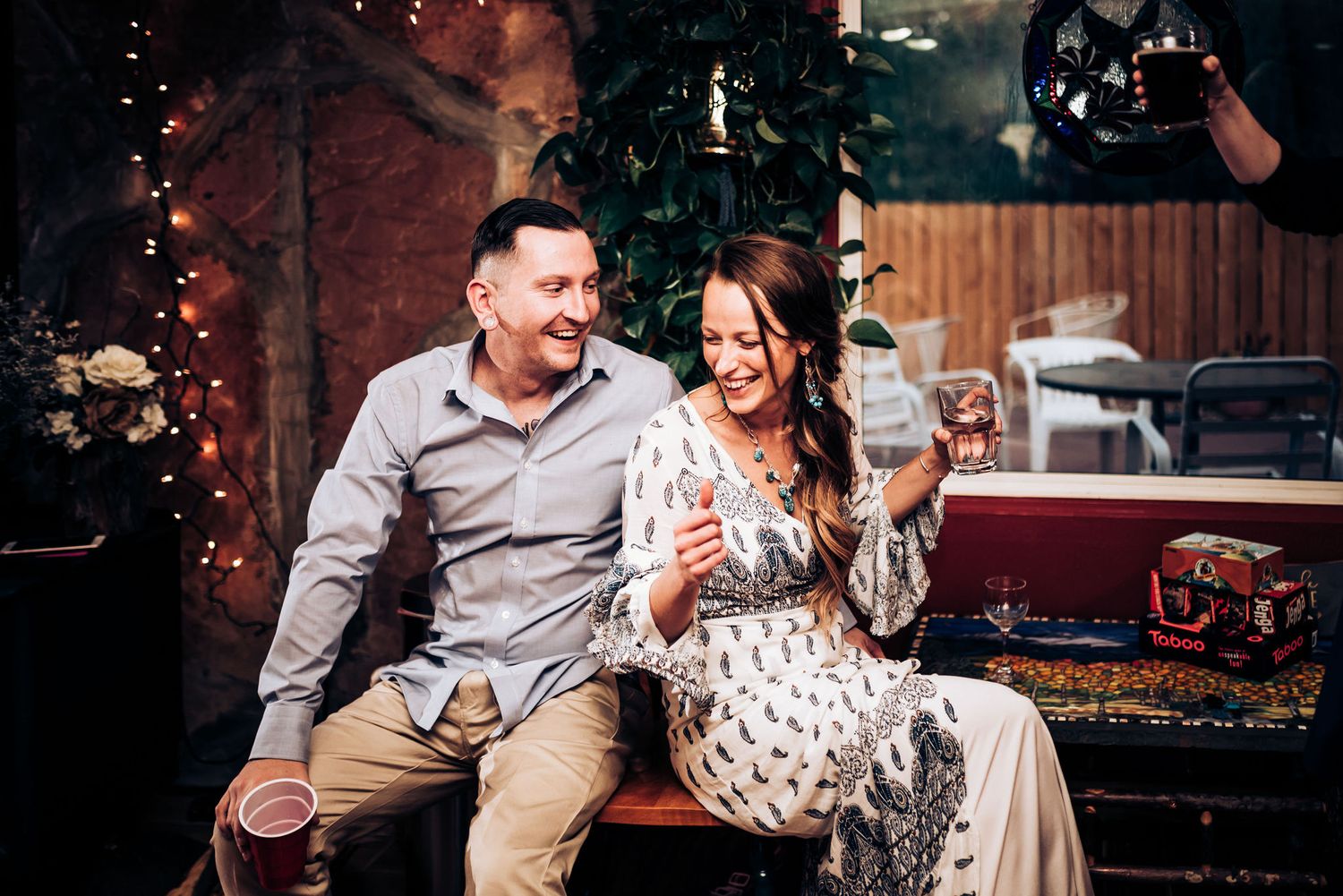 Couple relaxes on couch in rustic venue decorated with string lights.