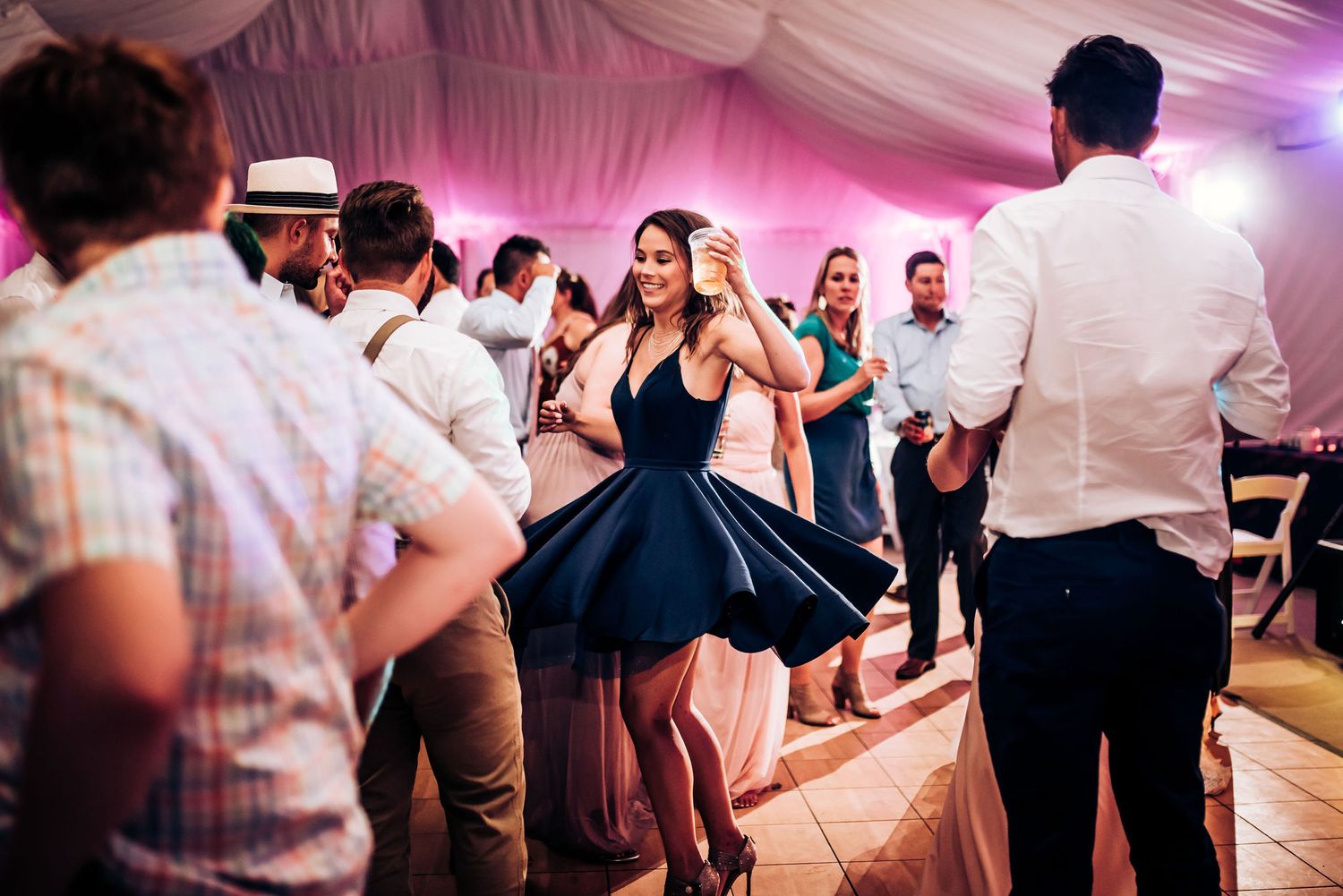 Wedding guests dancing and celebrating in a pink-lit reception tent.