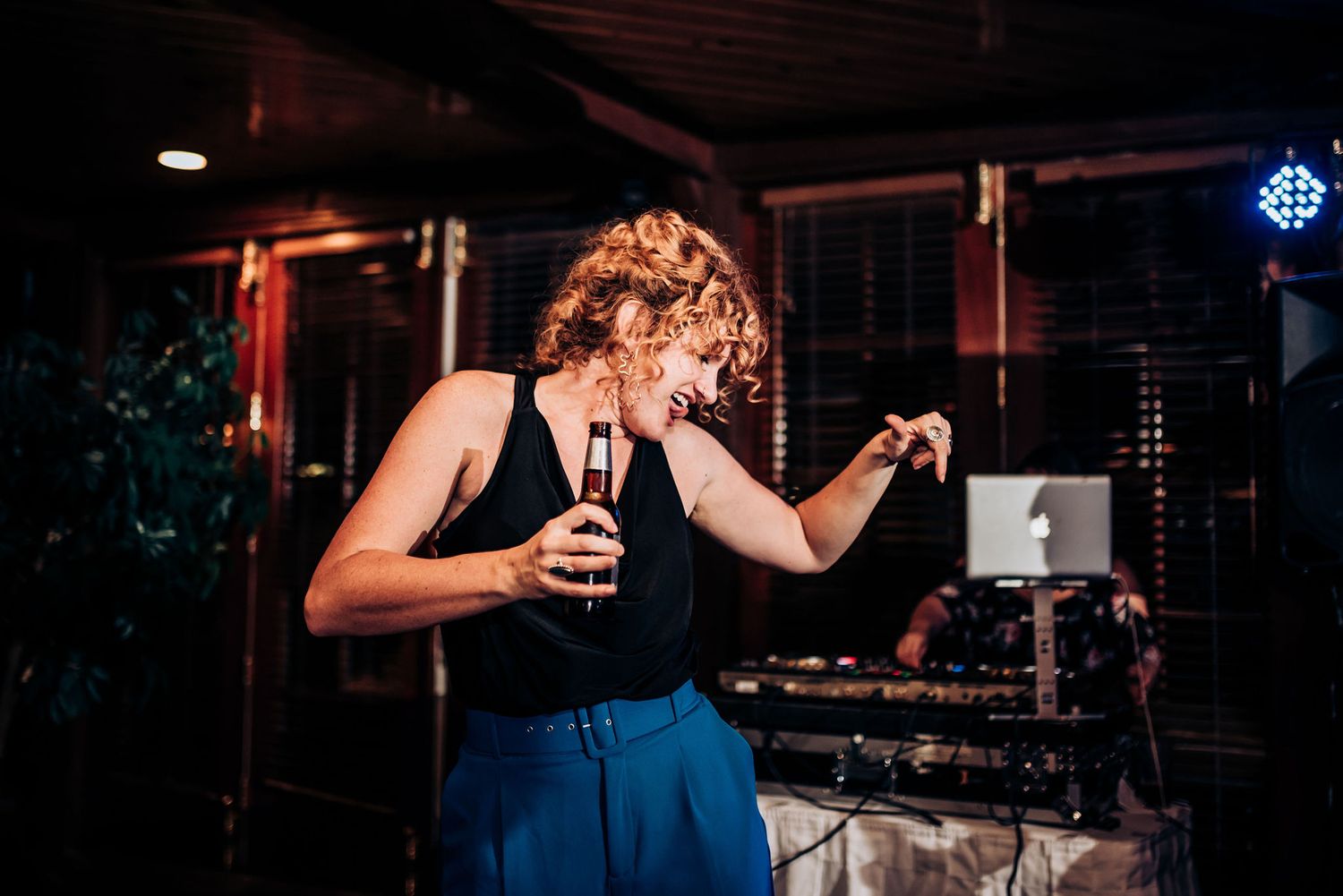 Person in blue pants dances solo with a drink in hand near DJ equipment.
