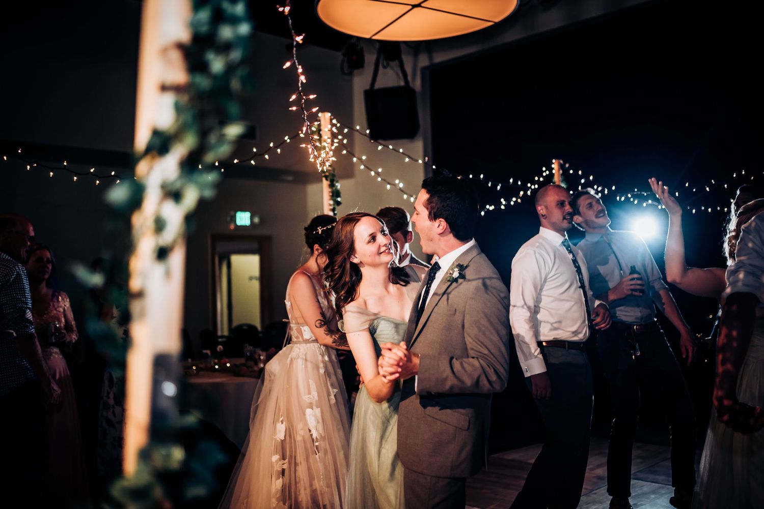 Wedding reception dance floor illuminated by string lights and warm overhead lamps.