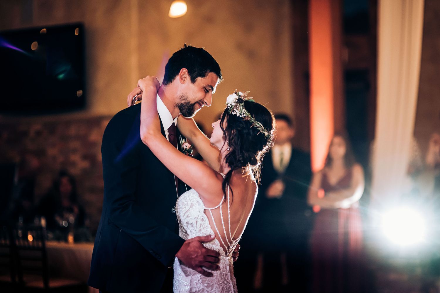 Newlyweds embrace during their first dance at an elegantly lit indoor reception.