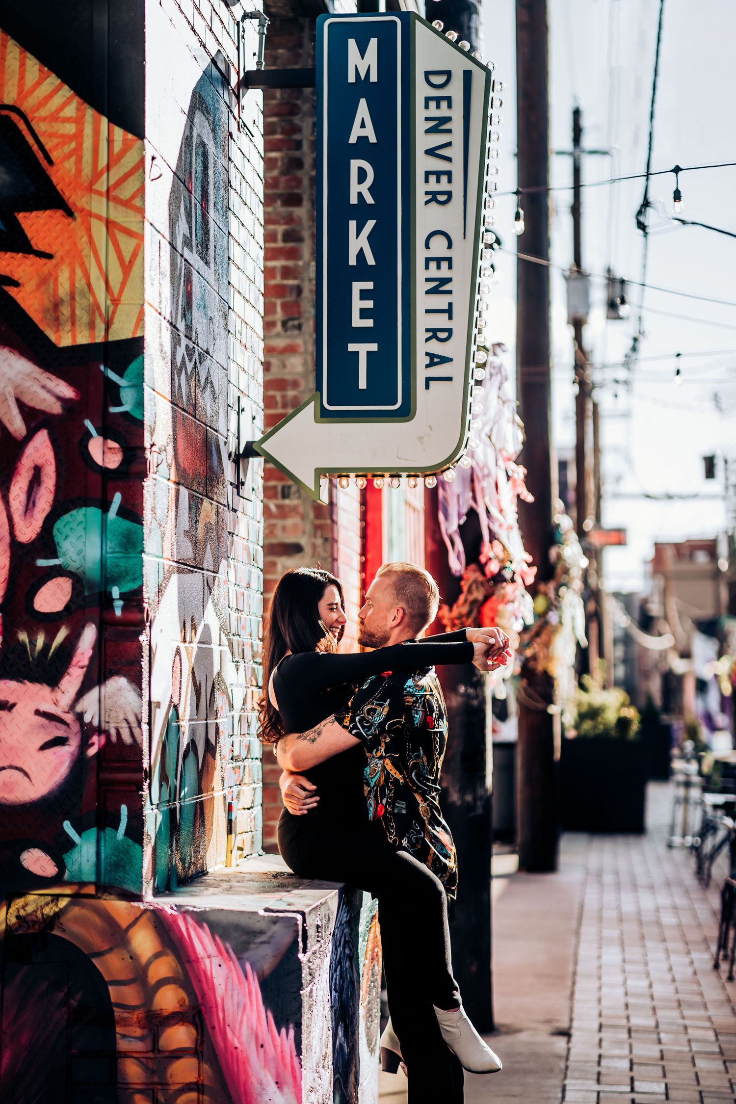 A couple sharing a romantic moment under a market sign with colorful street art in the background.