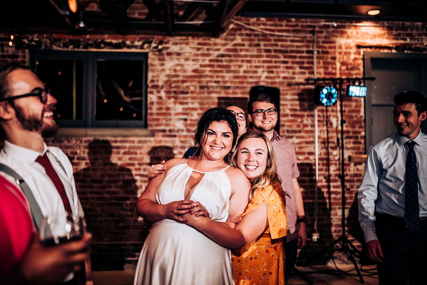 Guests share joyful moments during a wedding reception in an industrial-style venue with brick walls.