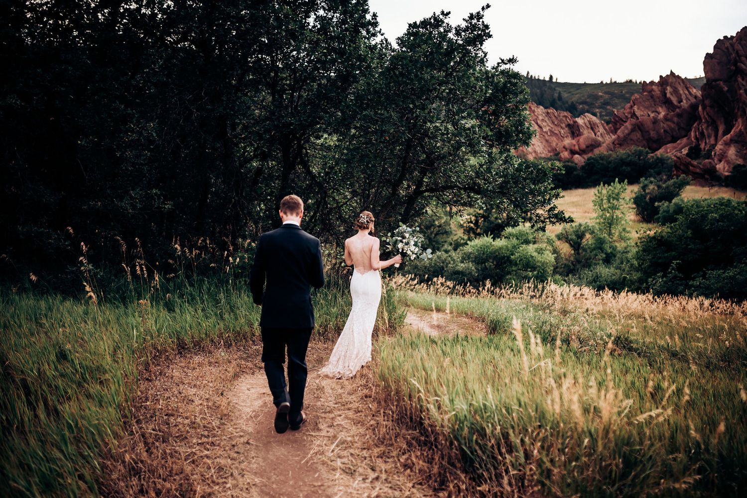 Couple walks down scenic trail with dramatic red rocks and natural landscape.