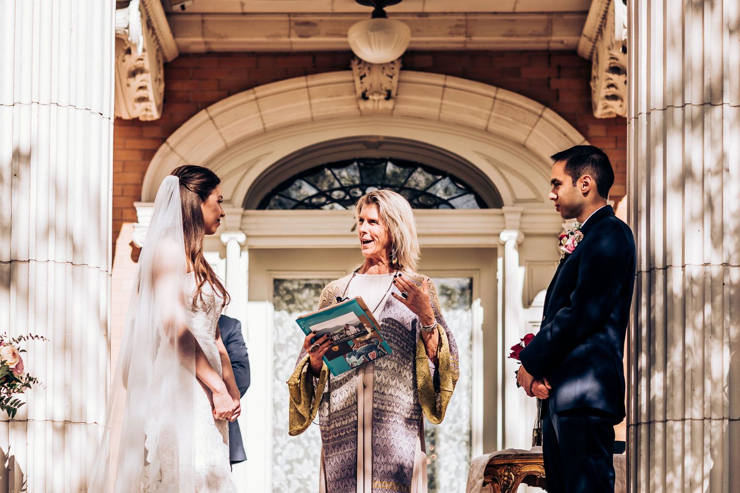 Wedding ceremony taking place under an ornate archway with classical architectural details.