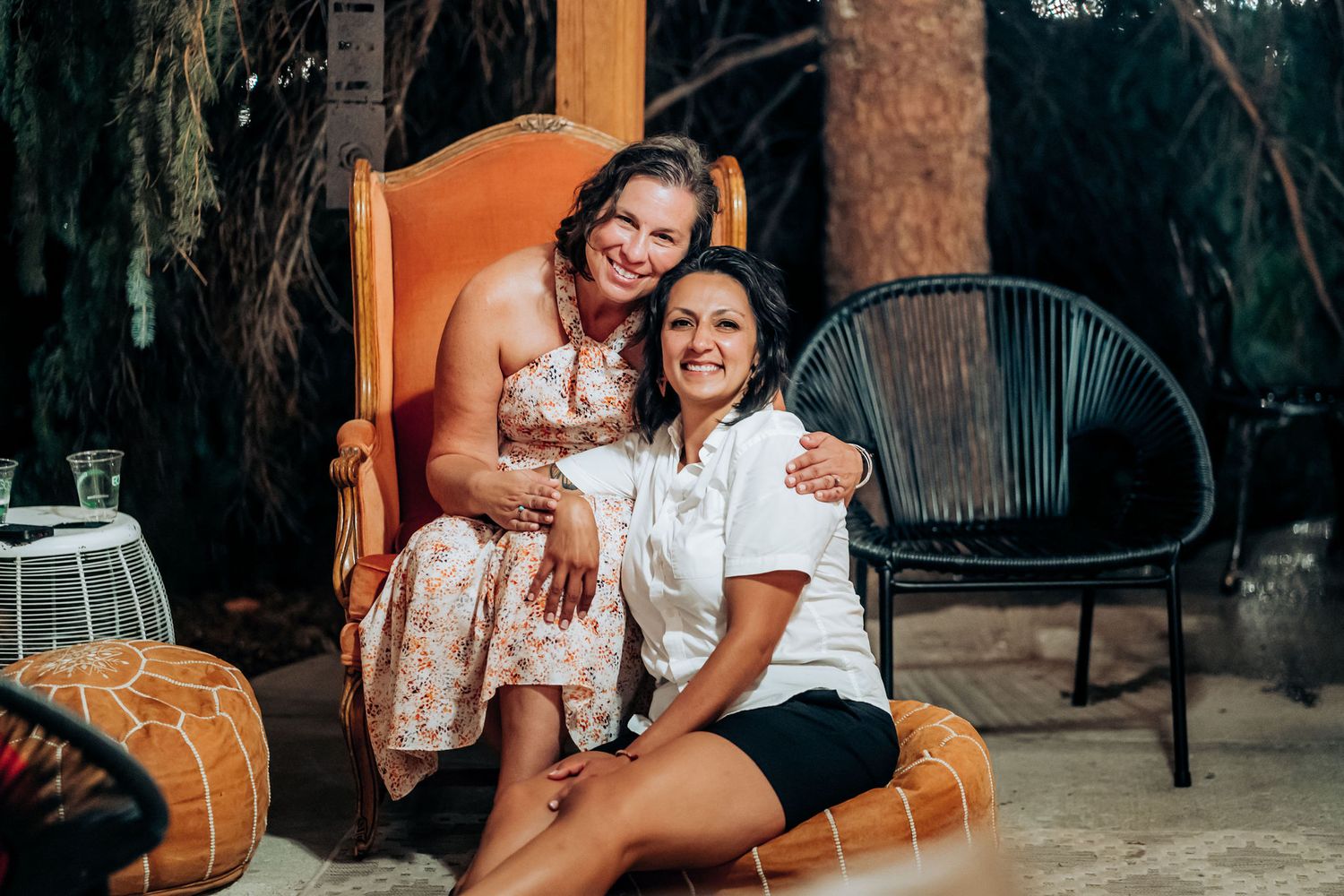 Two friends sharing a laugh while sitting on orange furniture outdoors.