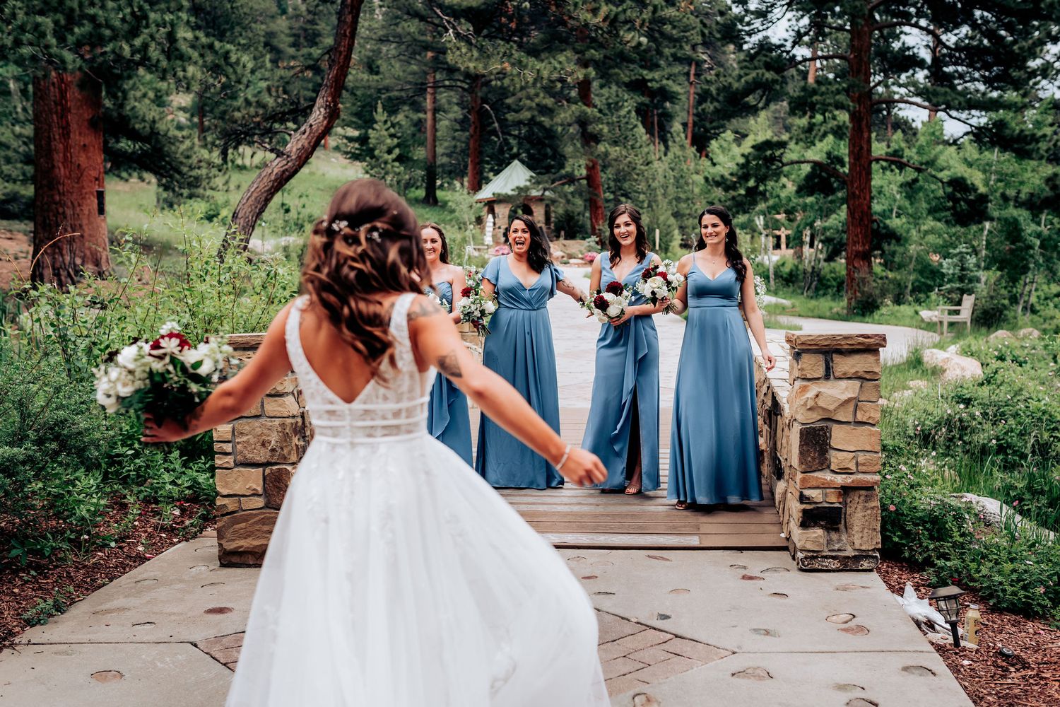 Wedding party in flowing blue dresses poses on a scenic stone pathway in the mountains.