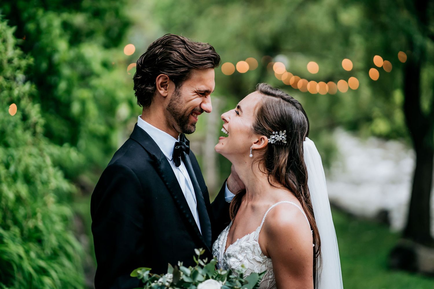 A candid moment of laughter between newlyweds in a garden setting with string lights.
