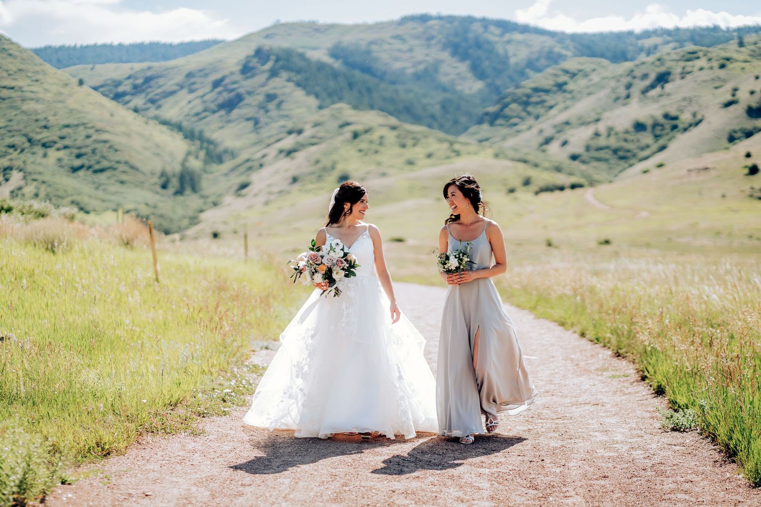 Two people in wedding attire walking and talking on mountain trail.