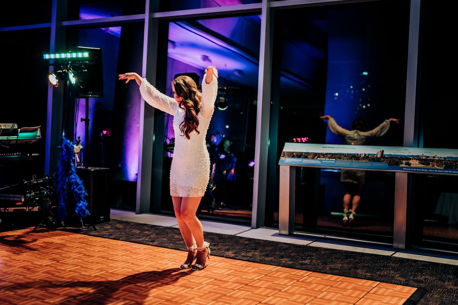A person in a white dress dances energetically on a wooden dance floor with blue lighting.