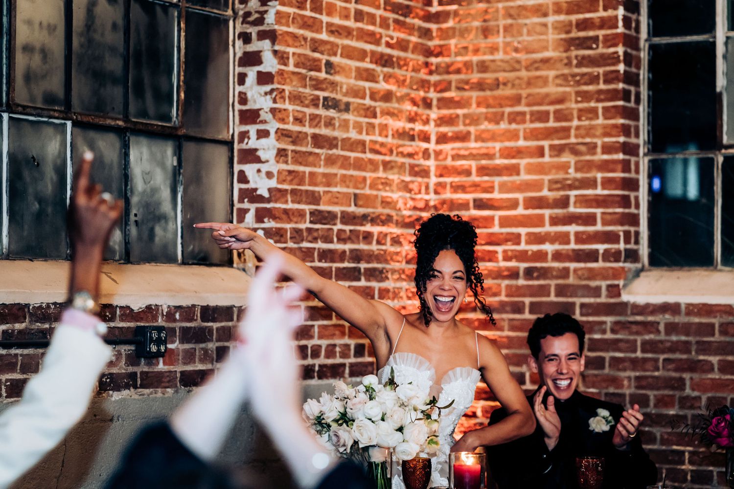 Wedding guests cheer and raise their hands during a celebratory moment at a reception.