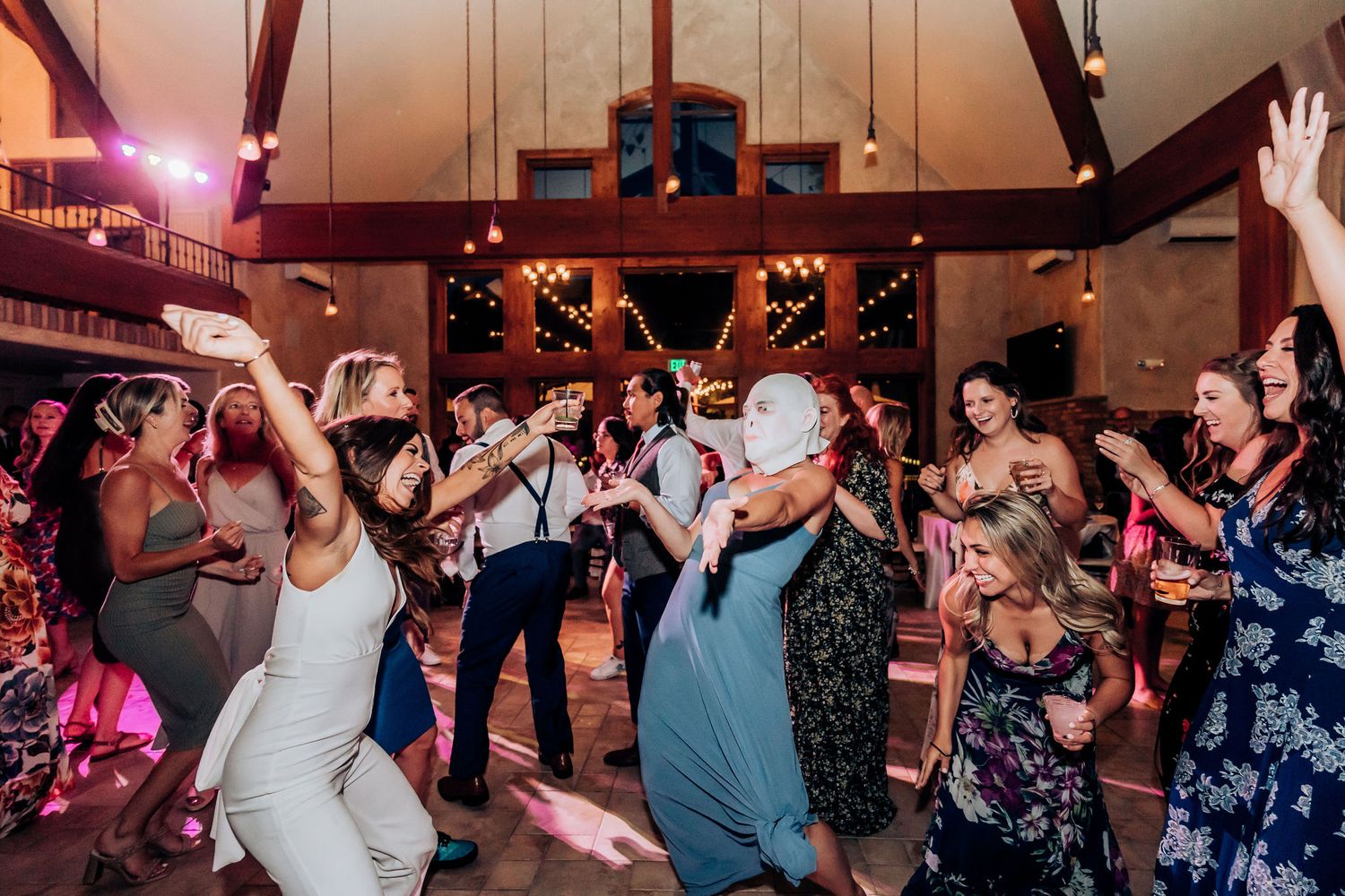 Wedding reception guests dancing enthusiastically in a rustic venue with exposed wooden beams.