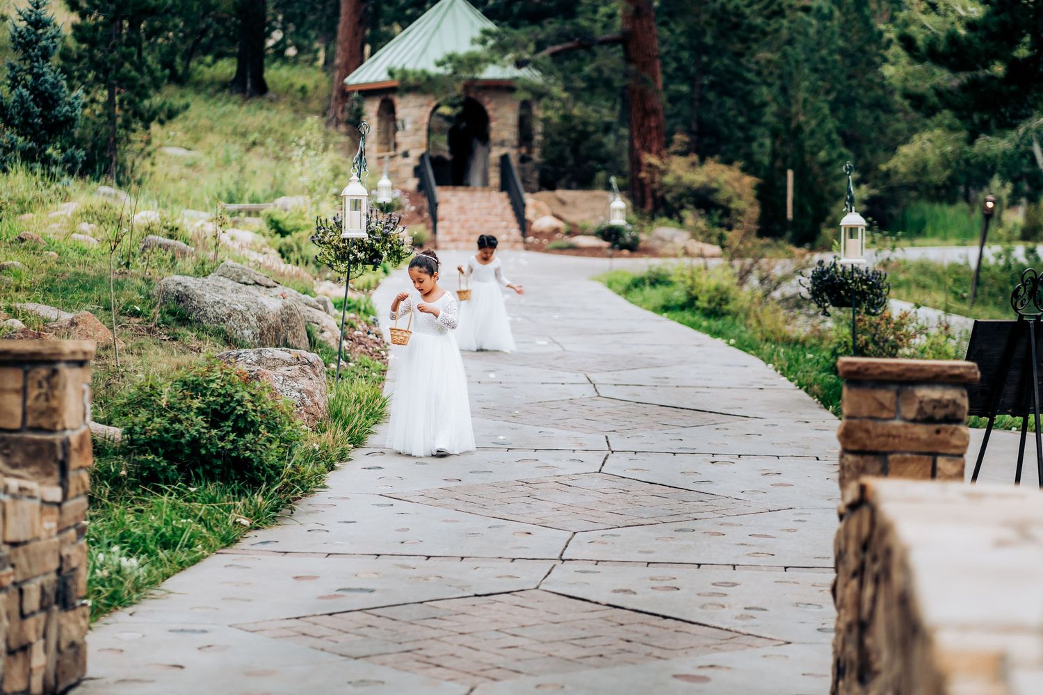 A flower-lined stone pathway leads to a gazebo during an outdoor wedding ceremony.
