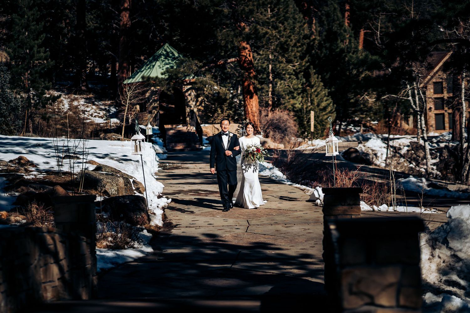 Wedding ceremony procession on a snowy mountain path with evergreen trees in background.