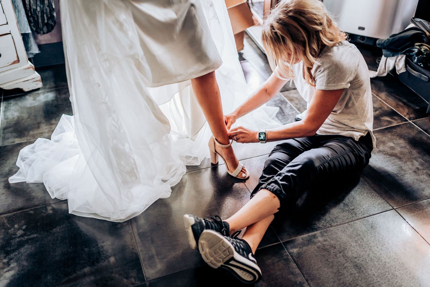 Someone helping with wedding shoe preparations while sitting on a dark floor.