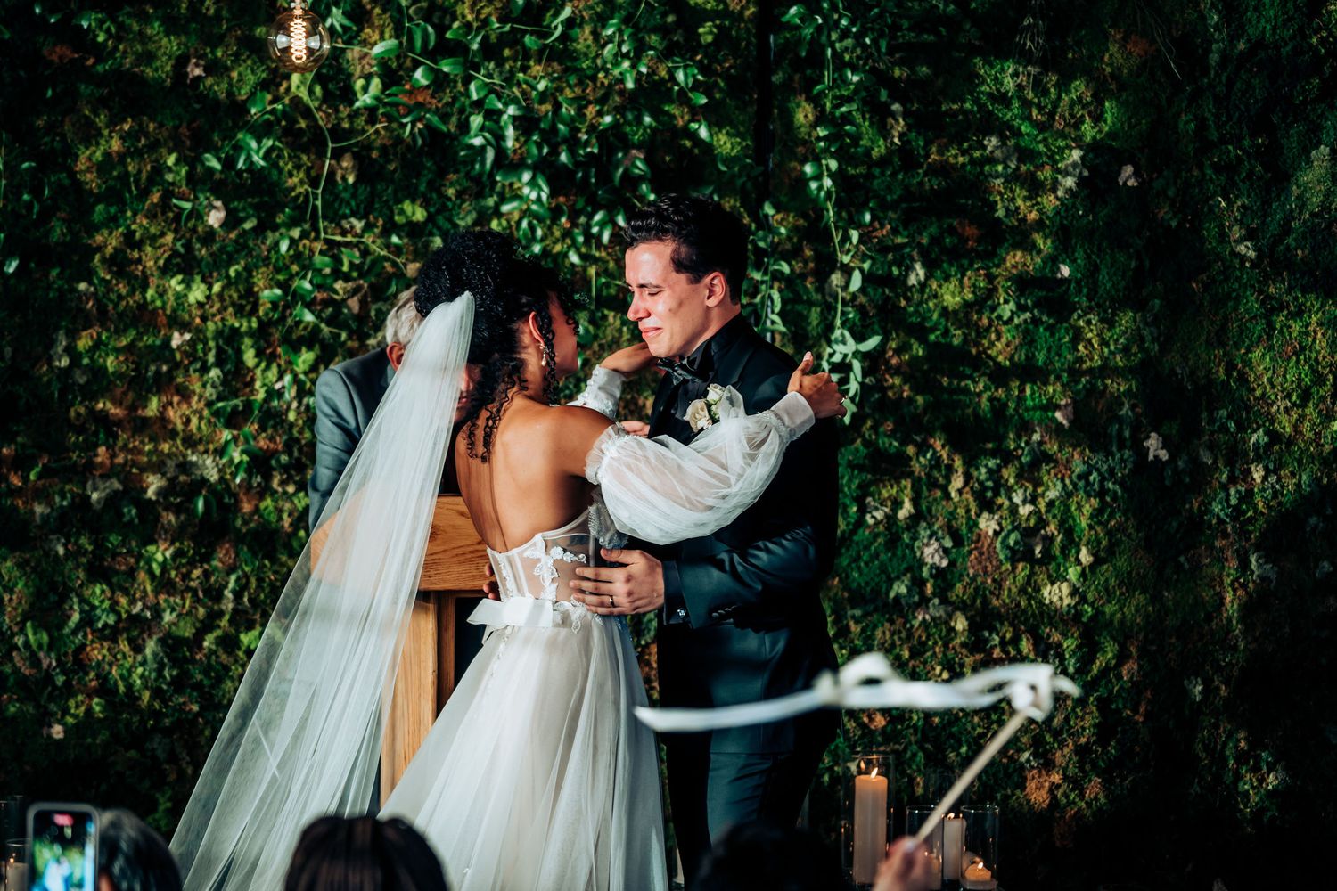 Elegant outdoor wedding ceremony with lush foliage wall and romantic lighting.