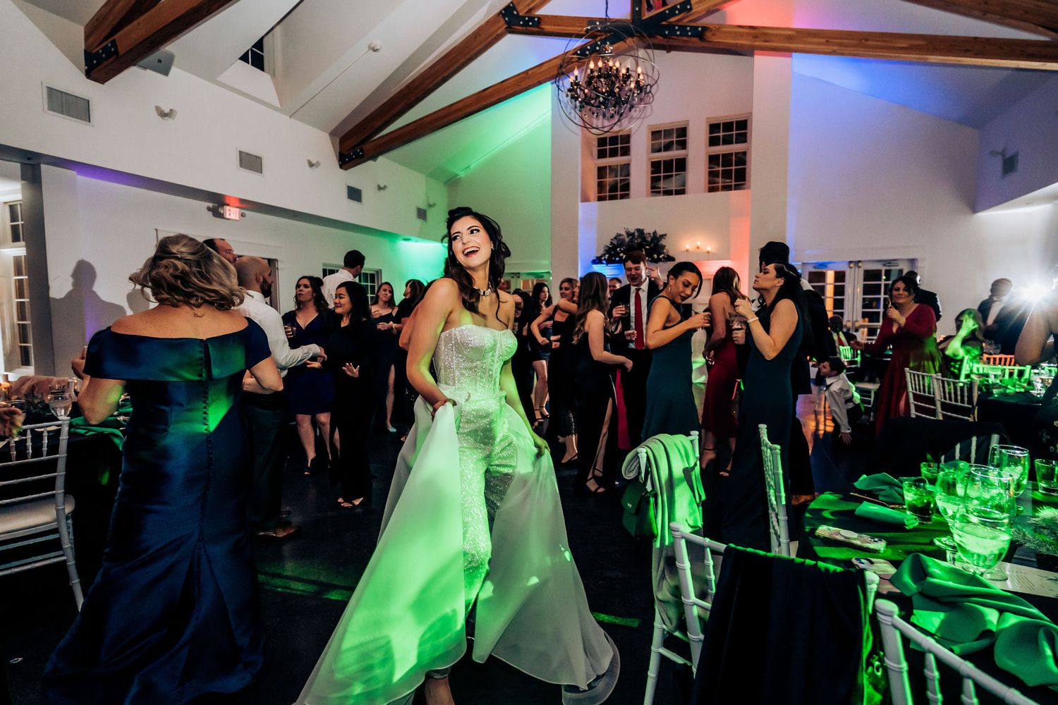 Wedding party dances in a venue with exposed beams and dramatic green lighting effects.