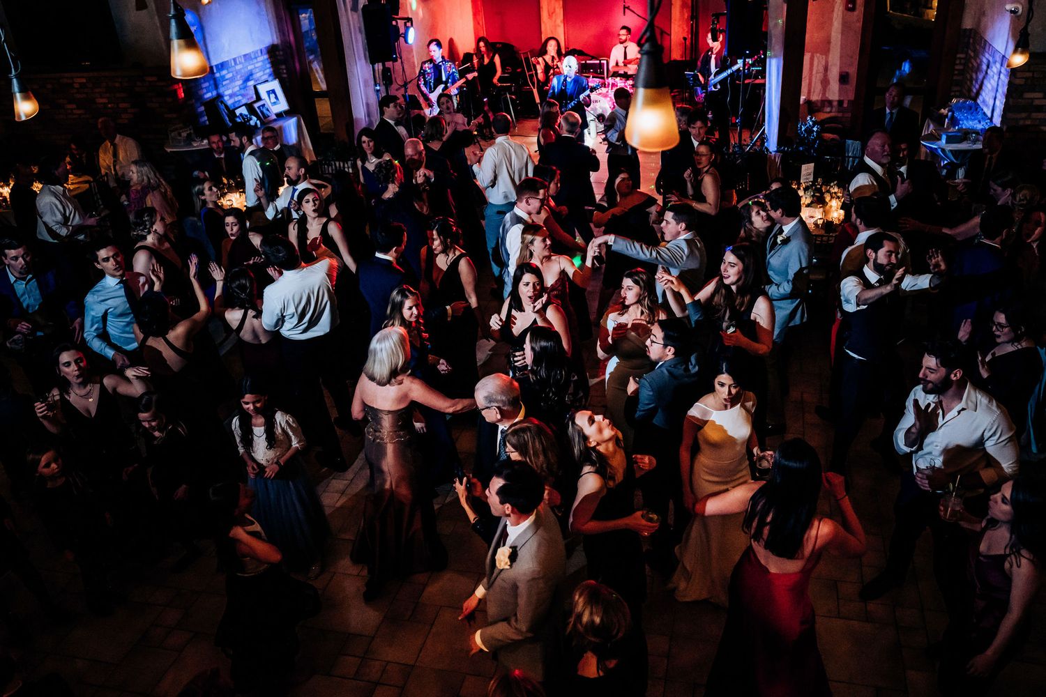 A crowded dance floor filled with party guests dancing under moody lighting at a wedding reception.