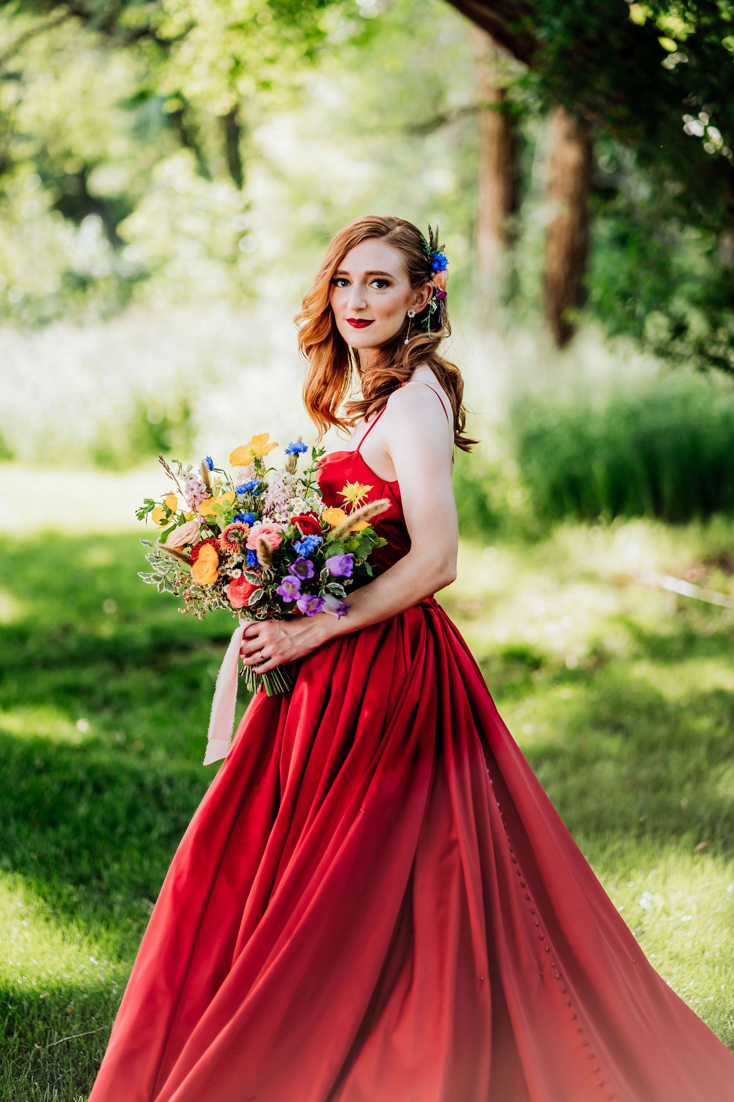 Red ballgown wedding dress with colorful wildflower bouquet in garden setting.