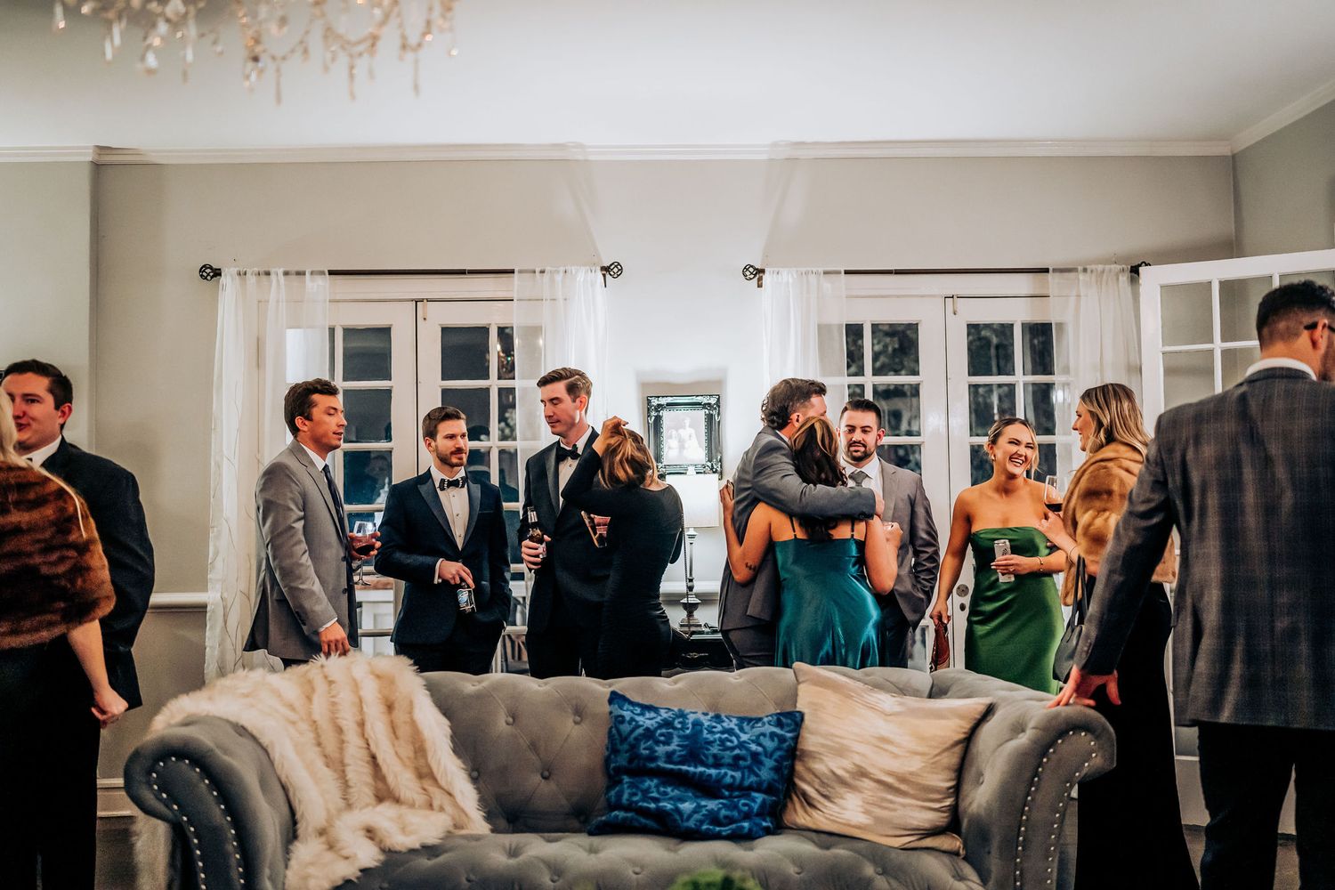 Guests mingling and socializing around a gray couch at an indoor event.