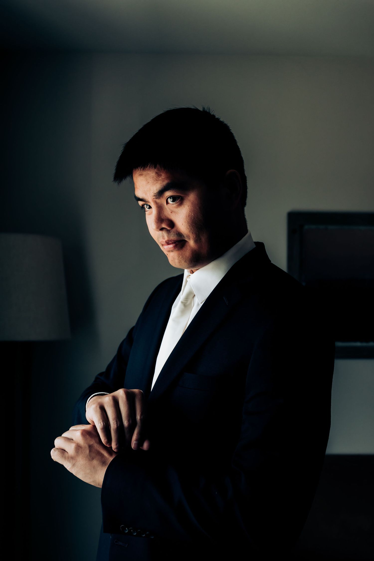 Groom in dark suit poses in dramatic side lighting for wedding portrait.