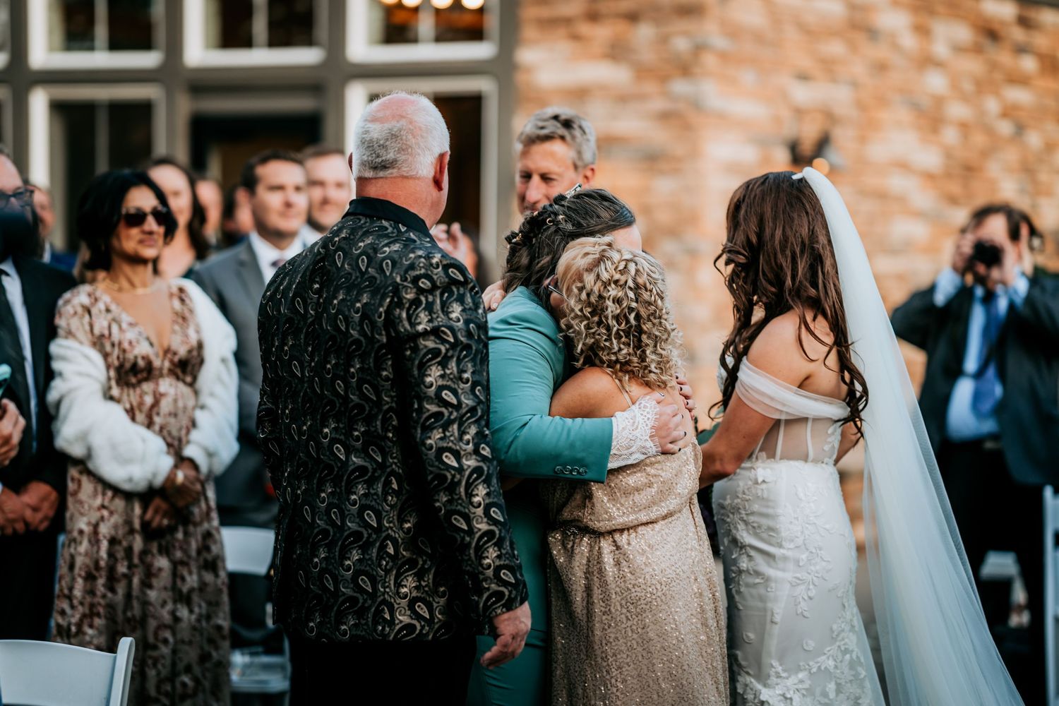 Emotional wedding moment as bride hugs family members at outdoor ceremony altar.