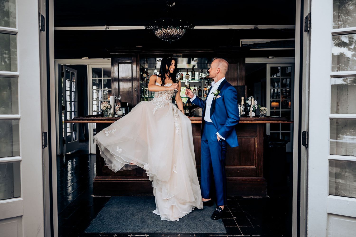 Elegant couple in wedding attire posing in front of dark bar interior.