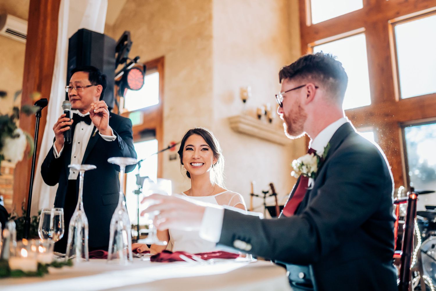 A speech is given during a wedding reception in an elegant room with high windows and warm lighting.