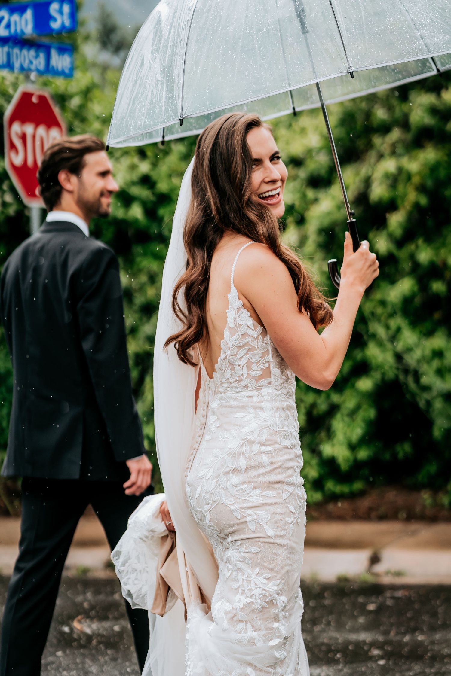 A rainy wedding day scene with a clear umbrella on a city street corner.