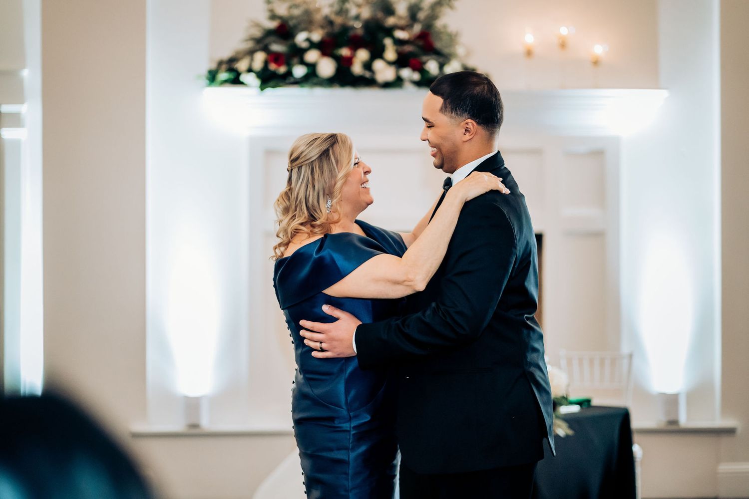 Couple shares intimate dance moment at wedding reception with decorative white pillars in background.
