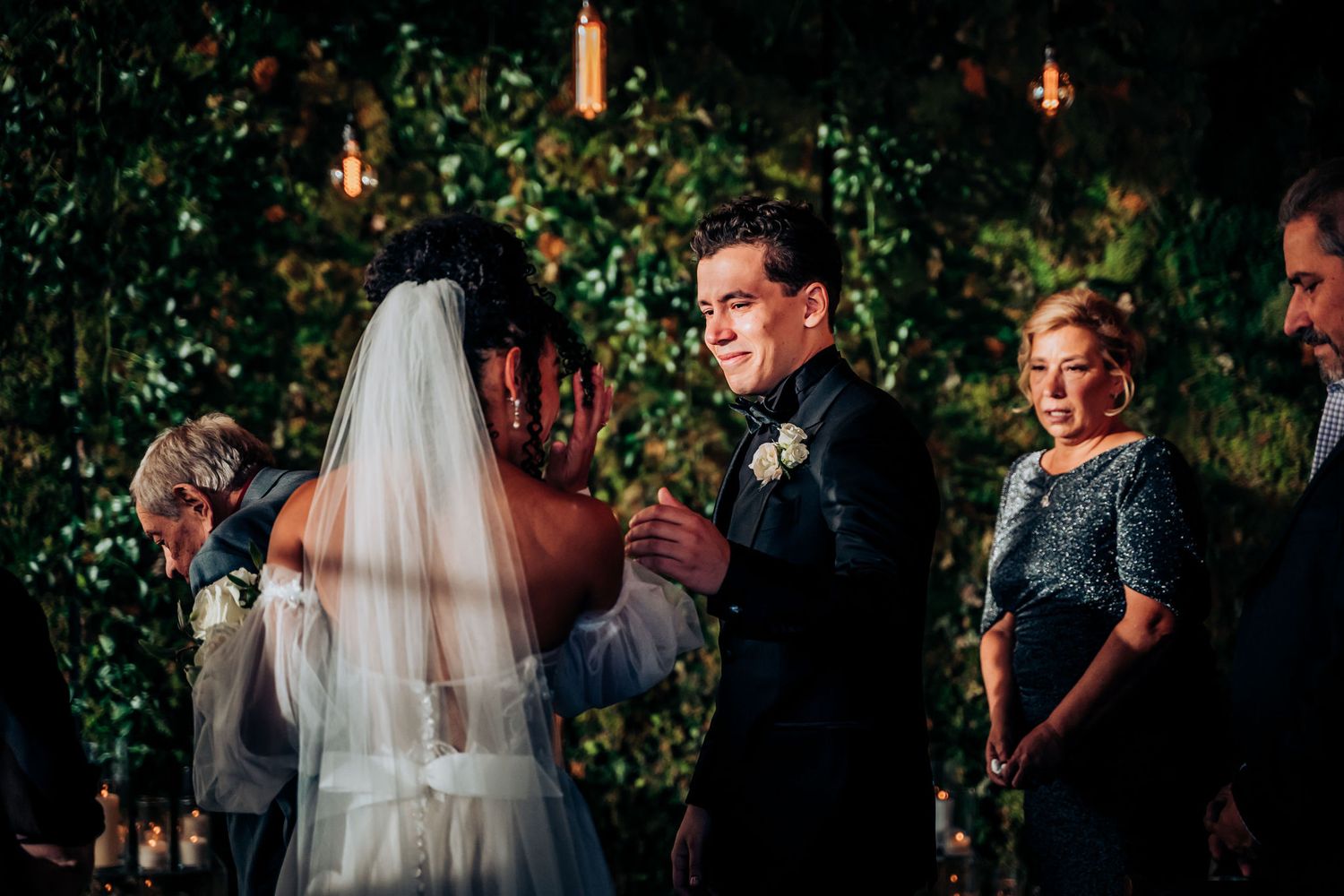 Wedding ceremony in front of a lush green wall with hanging pendant lights.