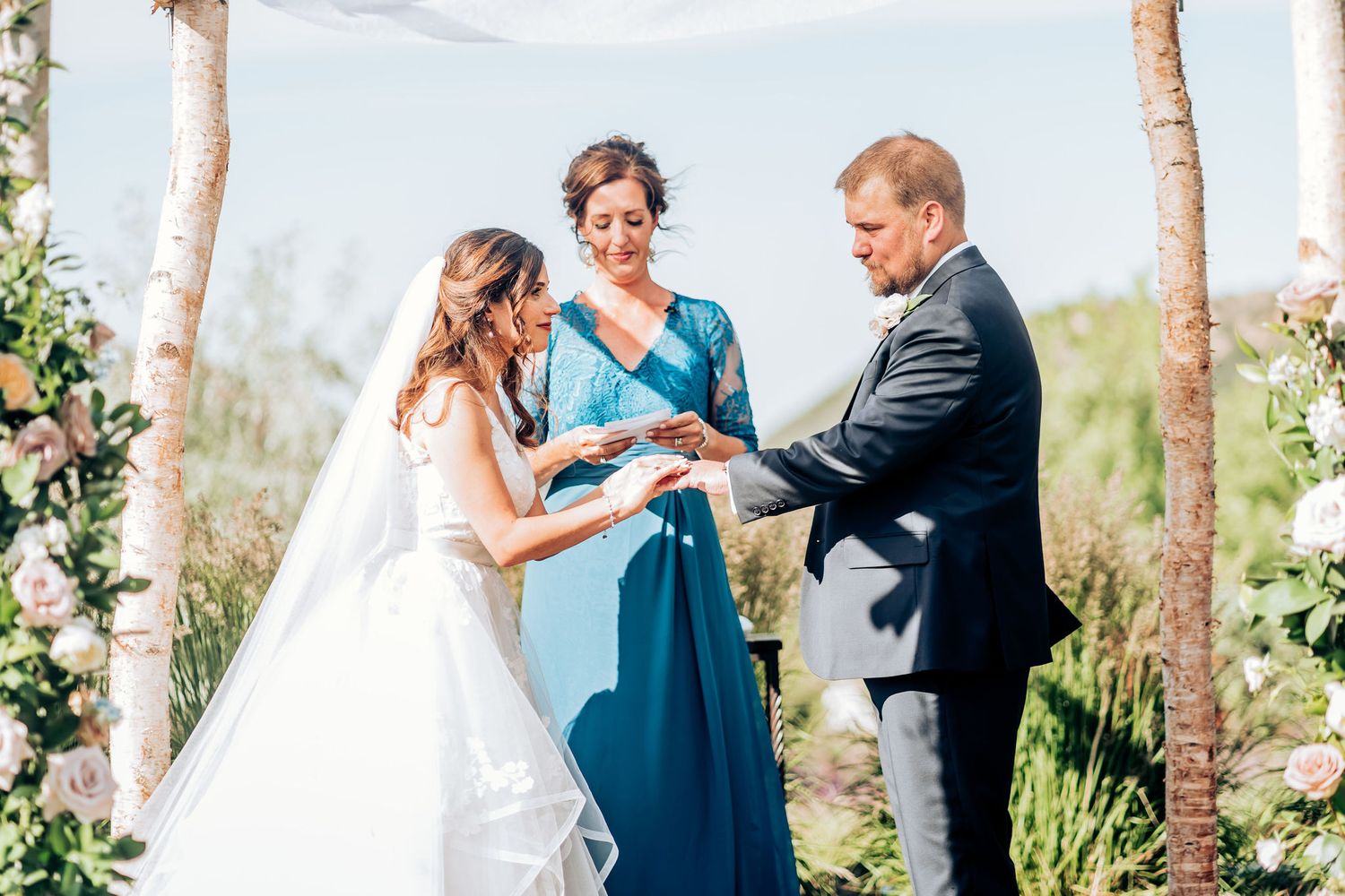 Ring exchange during mountain wedding ceremony under decorated wooden arch.
