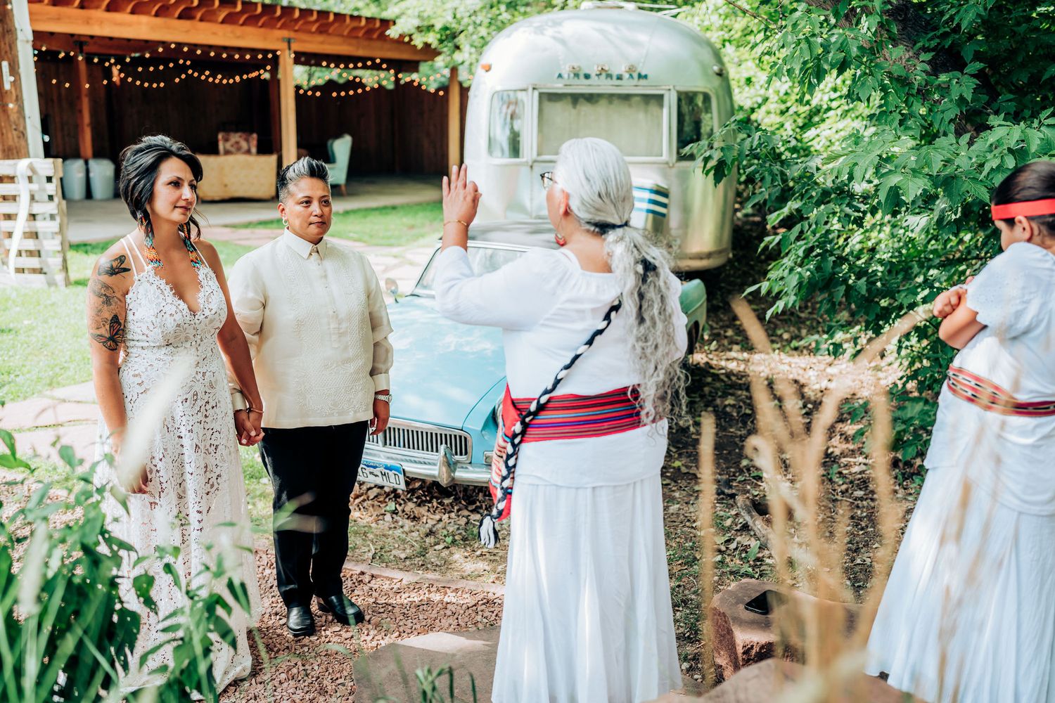 A vintage Airstream trailer serves as backdrop for a casual outdoor gathering in a garden setting.
