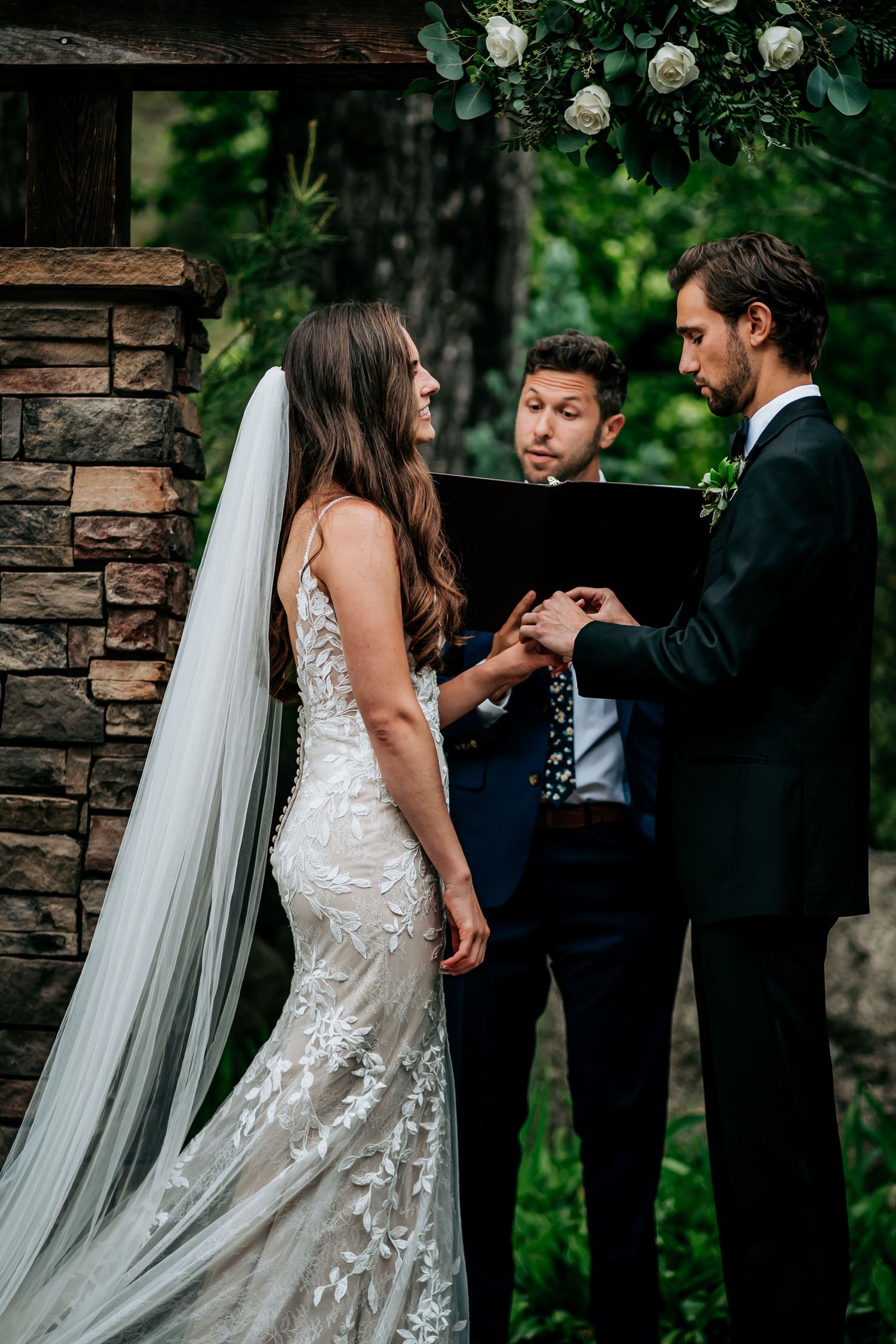 An intimate wedding ceremony takes place in front of a stone pillar surrounded by white roses.