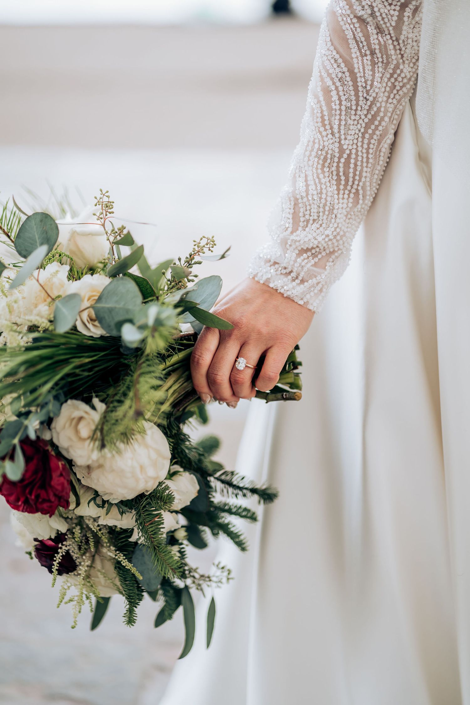 Close-up of lace wedding dress sleeve and bridal bouquet with white and red flowers.