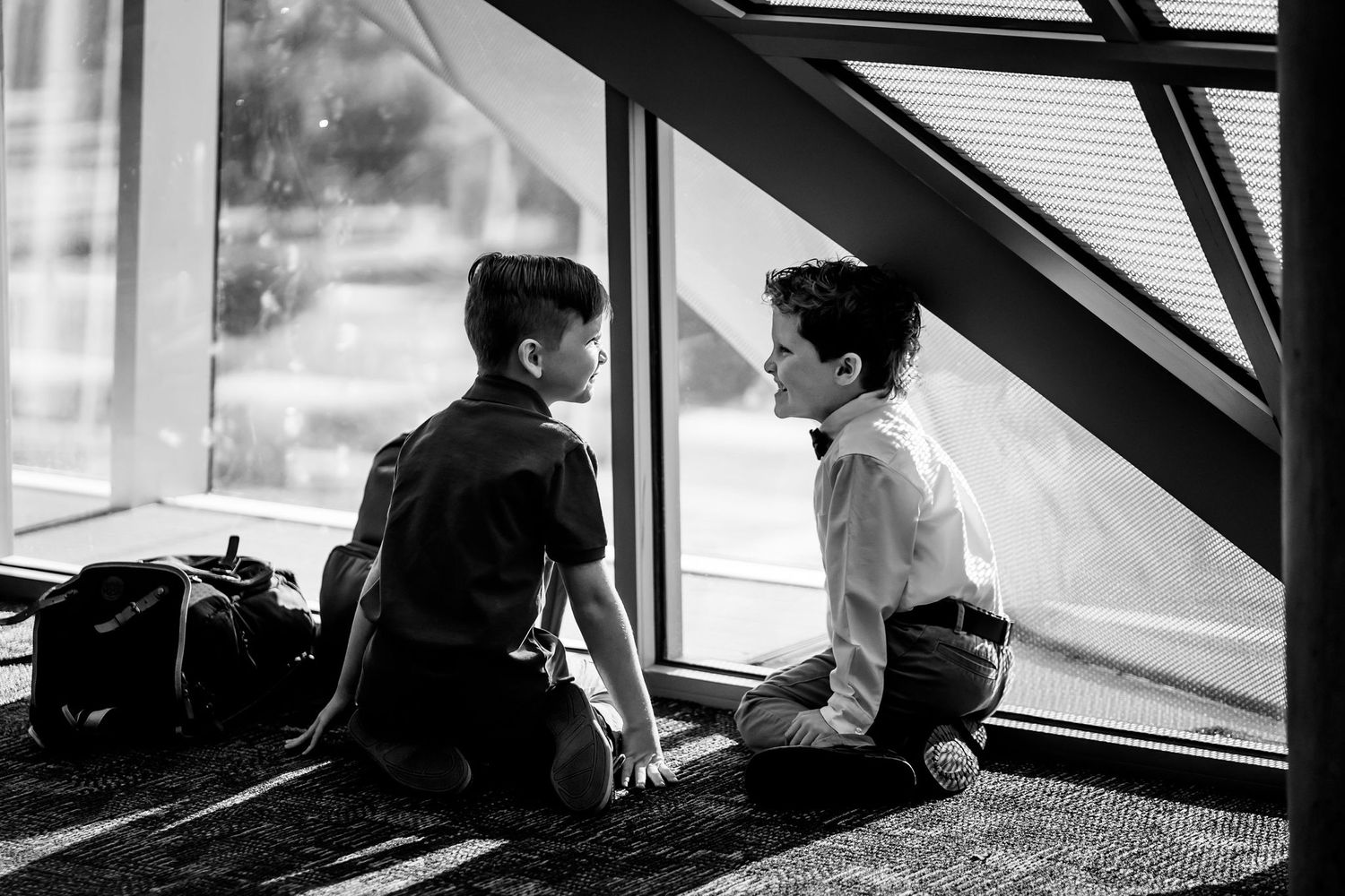 Two people sit by a large window having an intimate conversation in black and white.