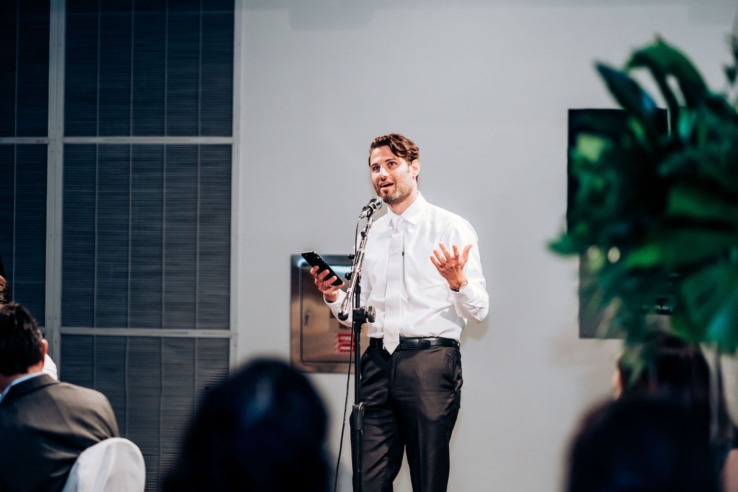A speaker in a white shirt gestures while giving a presentation to an audience.