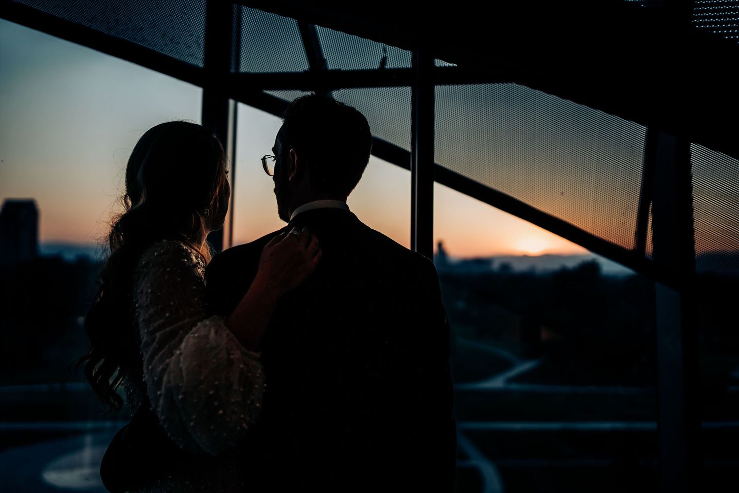 Silhouettes of a couple against sunset through large windows.