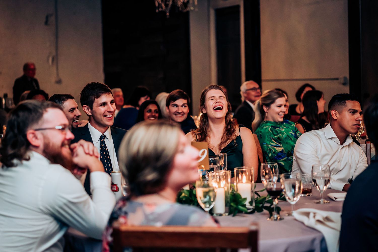 Wedding guests laugh and enjoy themselves during reception dinner at industrial venue.