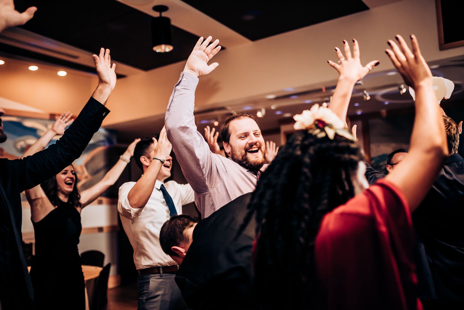 Energetic crowd with raised arms dancing and celebrating at an indoor event.