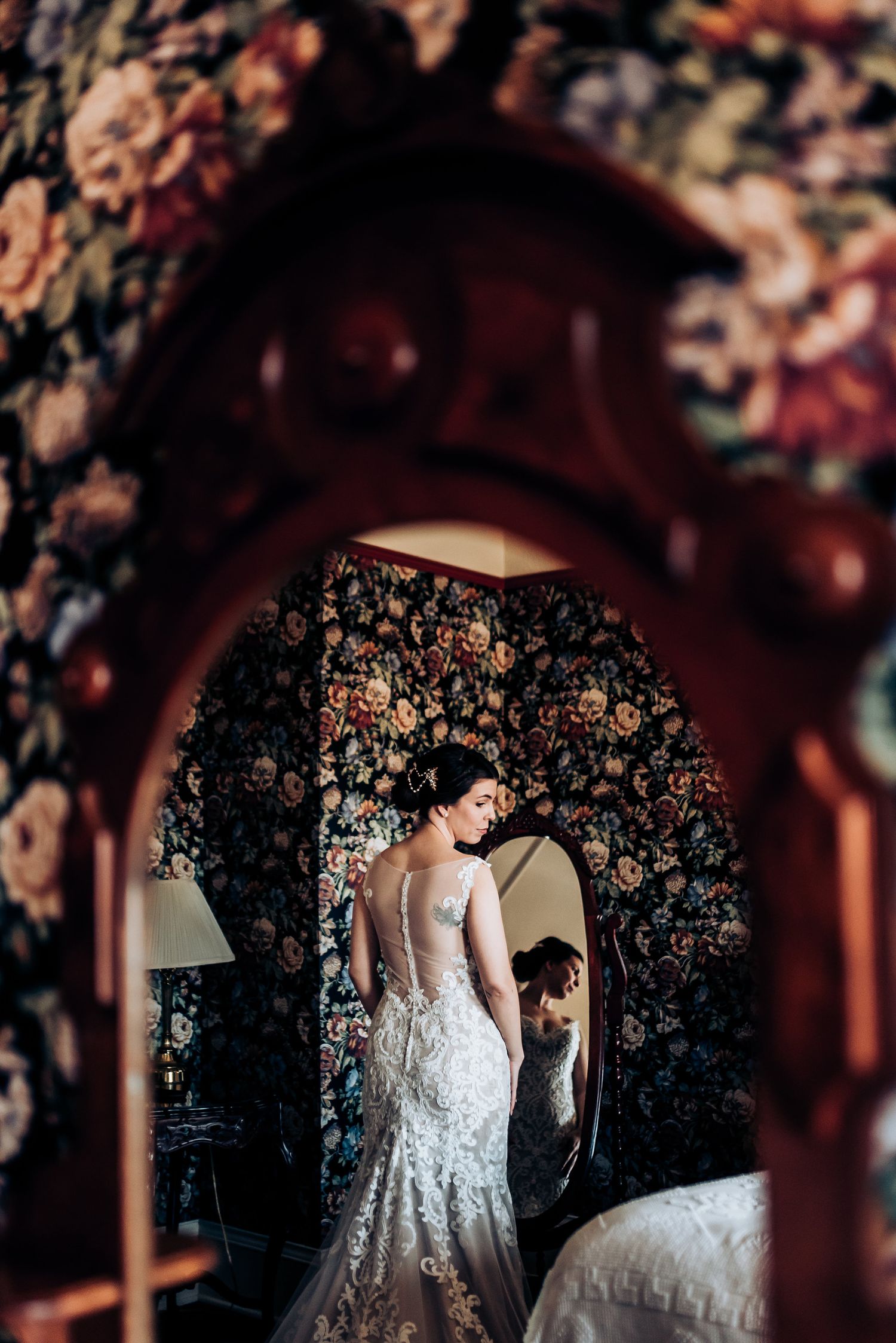 A wedding dress silhouette framed through an archway with vintage floral wallpaper background.