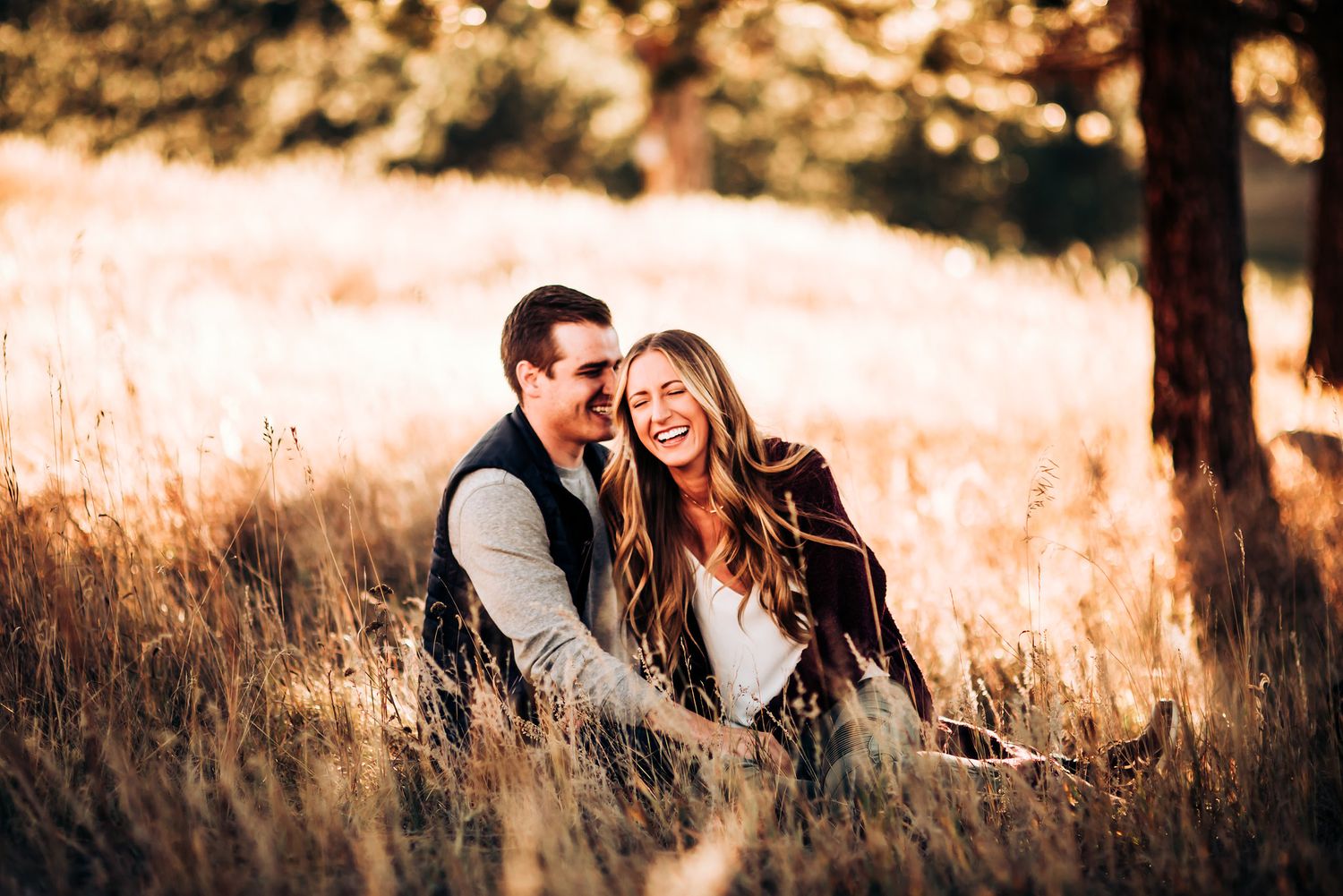 A couple sharing laughter while sitting in a sunlit meadow during golden hour.