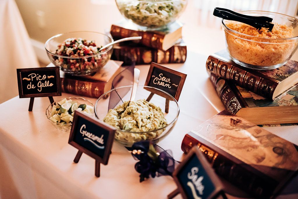 Buffet table with various dishes and small chalkboard labels on decorative stands.