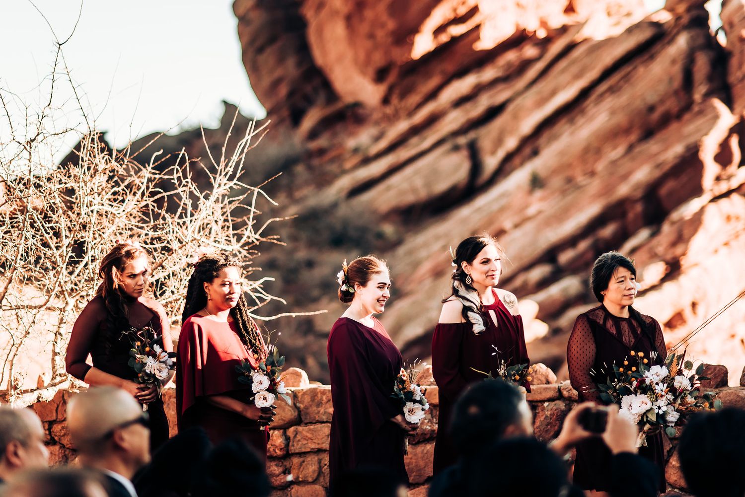 Wedding party stands against dramatic red rock formations during an outdoor ceremony.